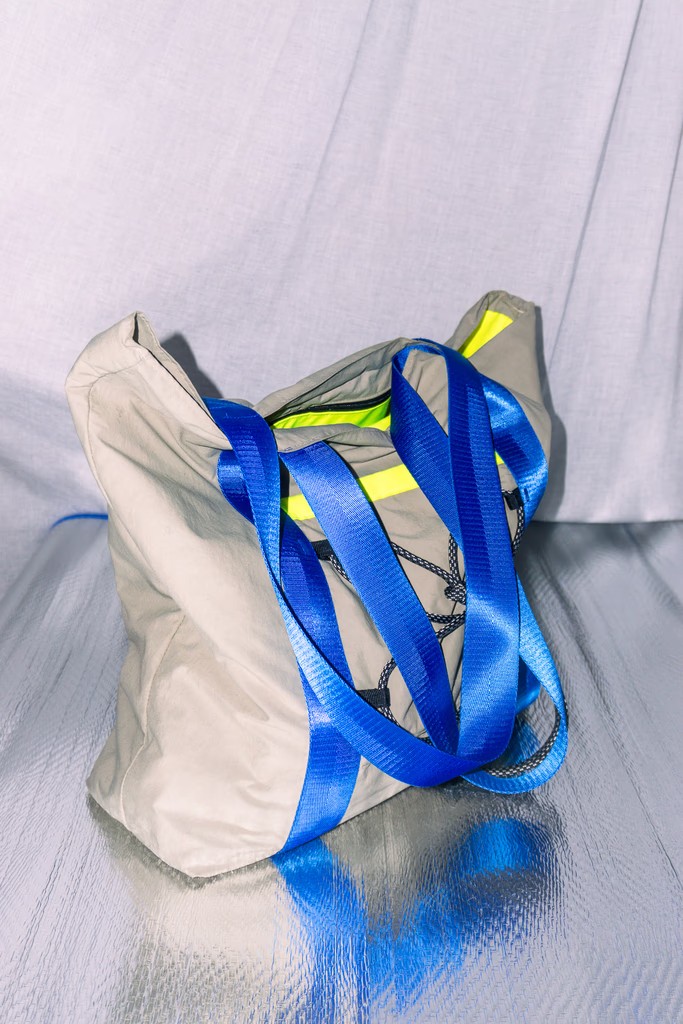 Beige technical tote with electric blue straps and bungee cord on a reflective surface