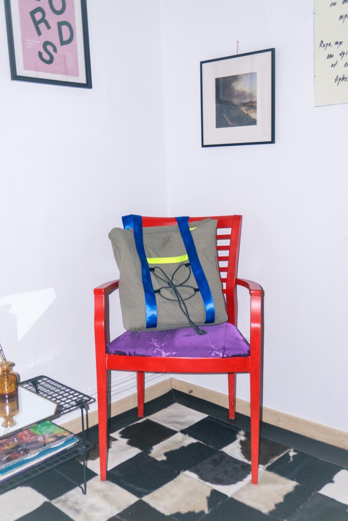 Grey canvas tote with blue straps and a lime stripe resting on a red wooden chair